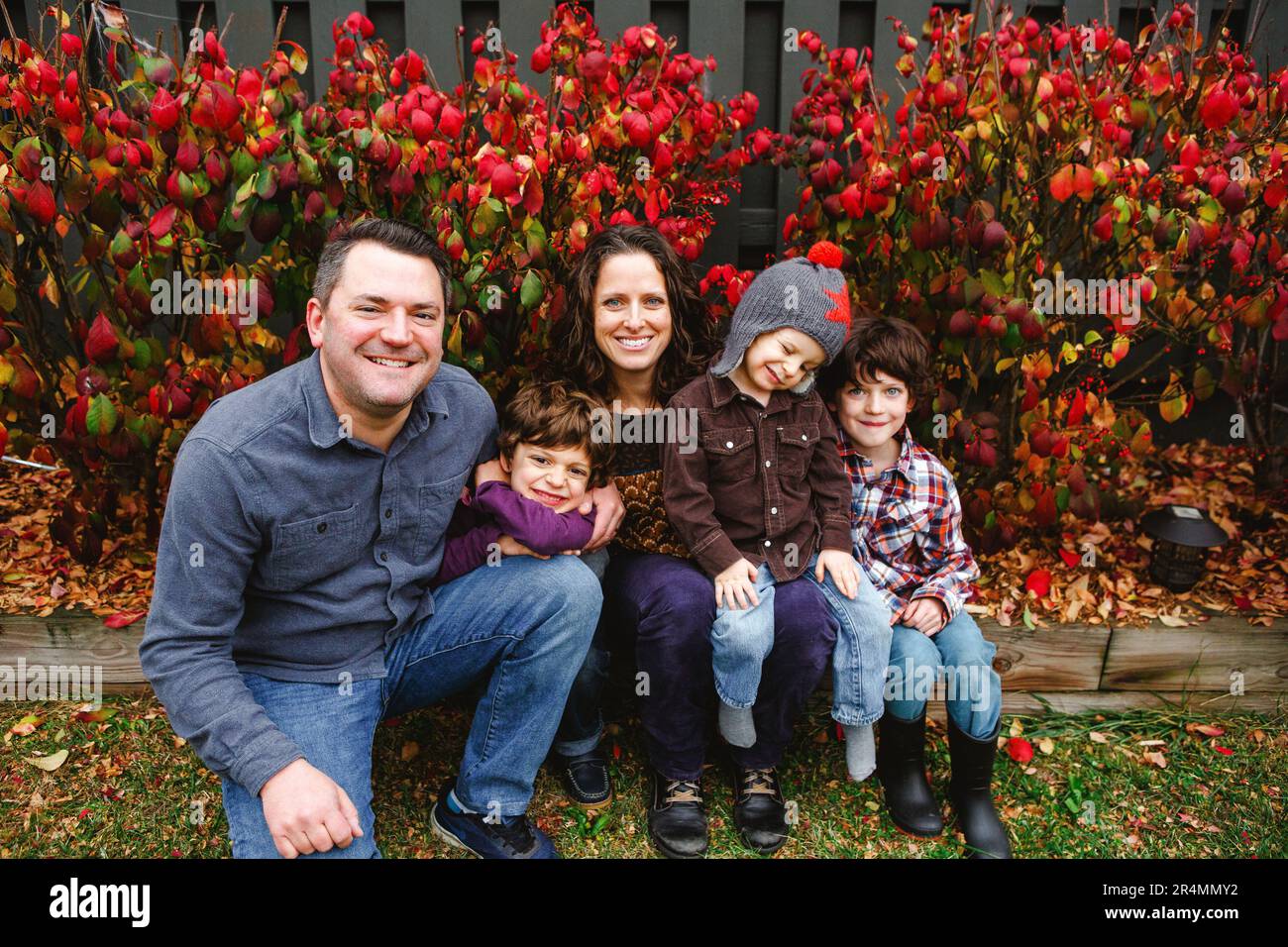 Una famiglia sorridente siede insieme sul ceppo di legno davanti alle foglie rosse Foto Stock