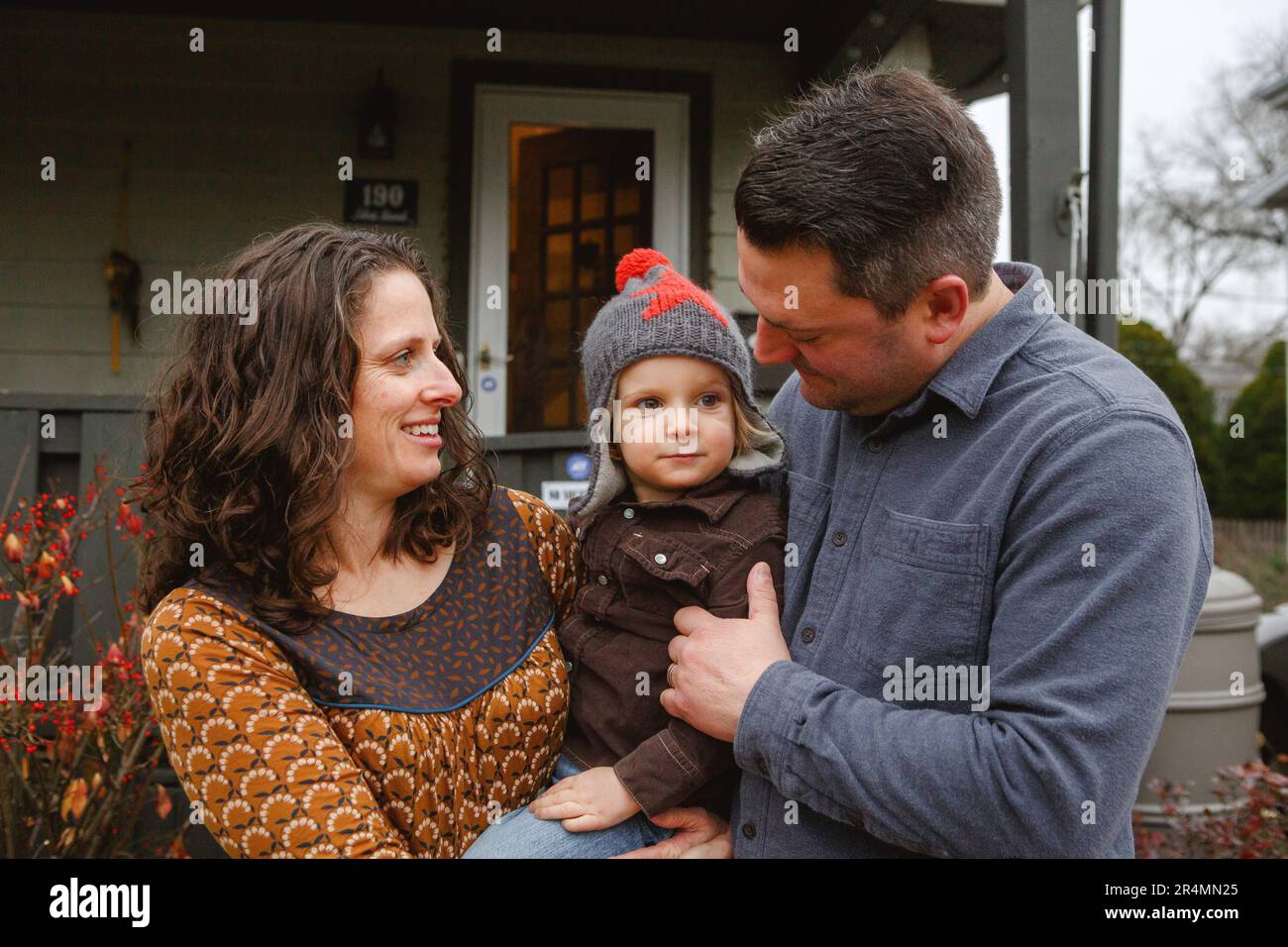 Una mamma e un papà amorevole culla un ragazzino tra loro di fronte a casa Foto Stock