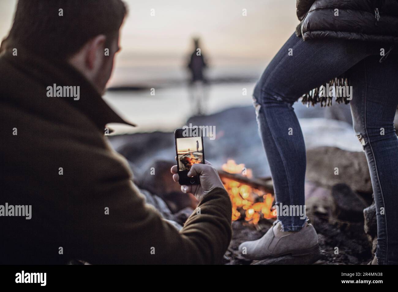 Un uomo scatta una foto di un falò con il suo cellulare o smartphone Foto Stock