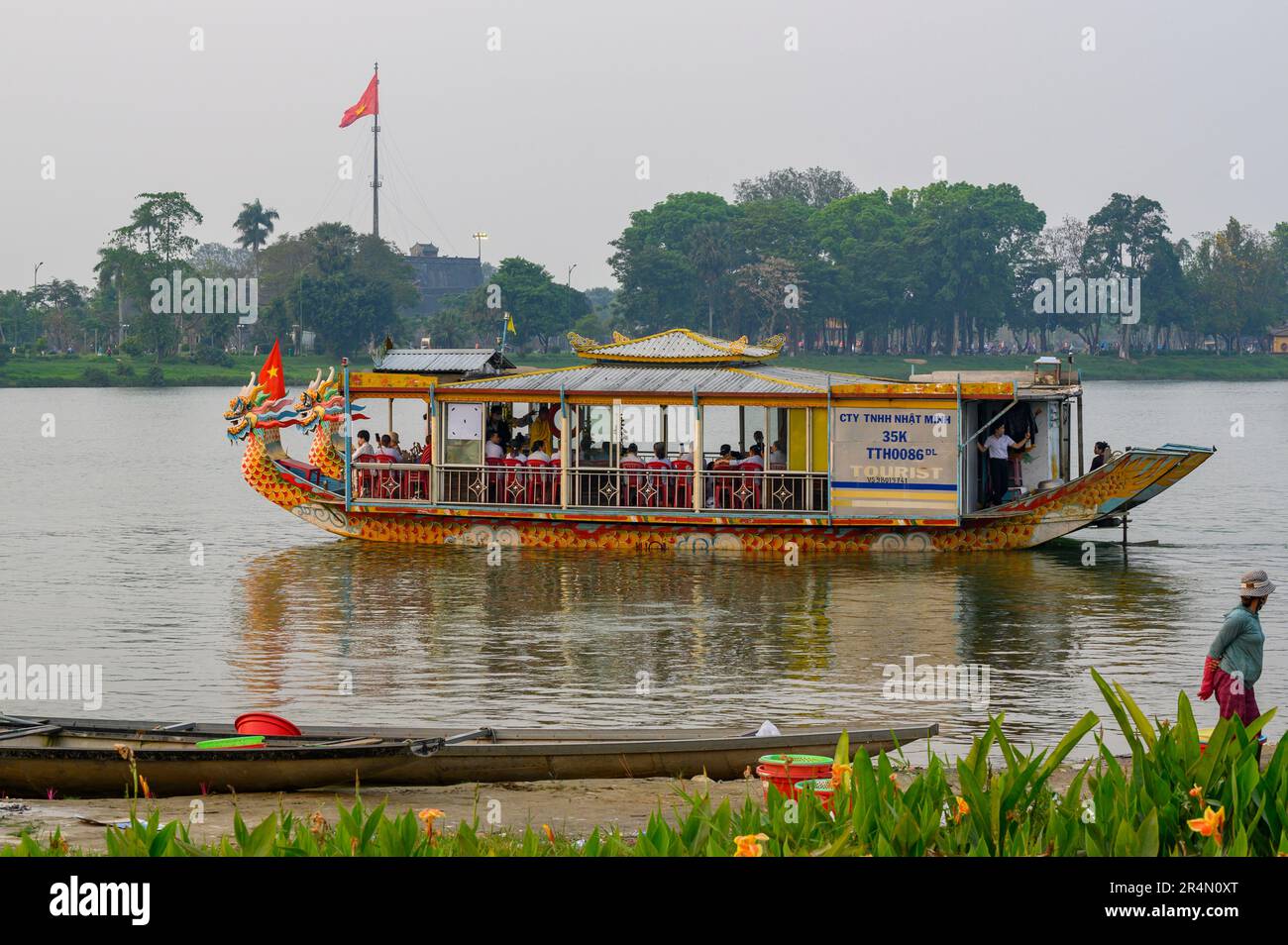 I turisti in una barca a drago navigano lentamente oltre la torre della bandiera della Cittadella alla luce del sole serale sul fiume profumo a Hue, Vietnam. Foto Stock