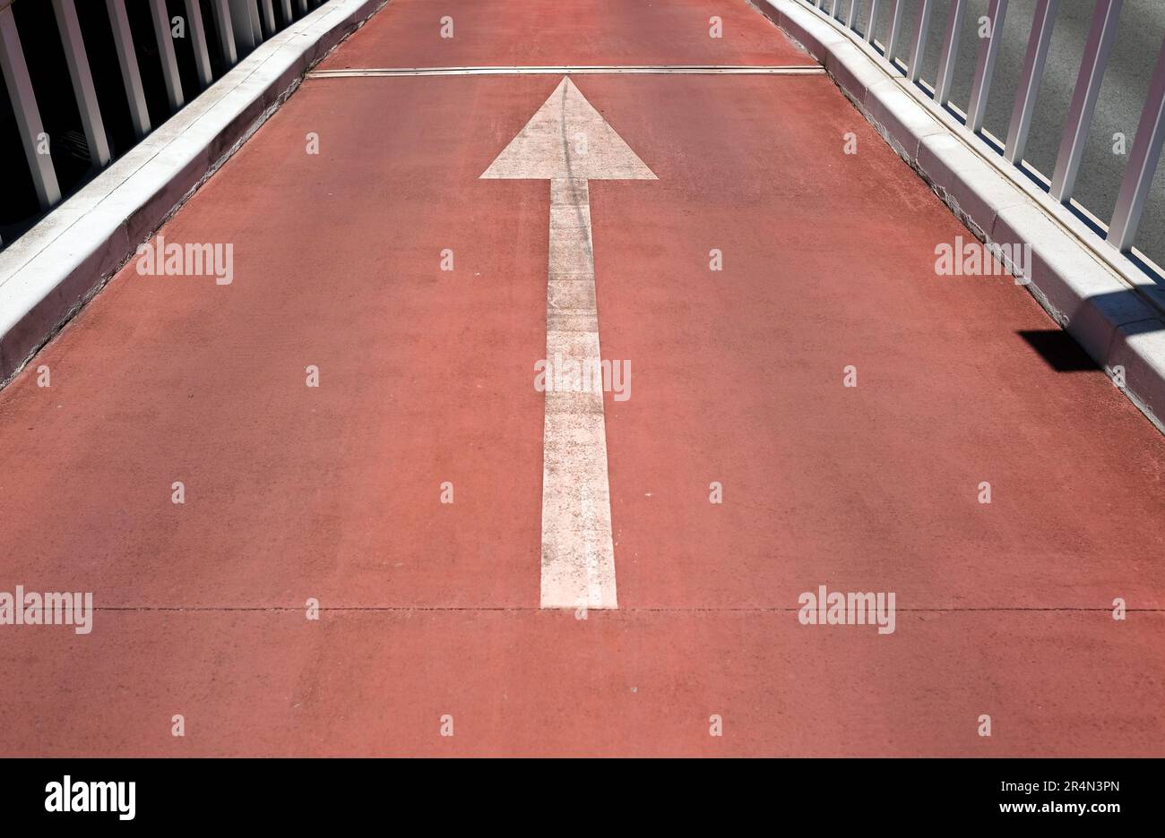Freccia bianca che punta in avanti su una strada rossa Foto Stock