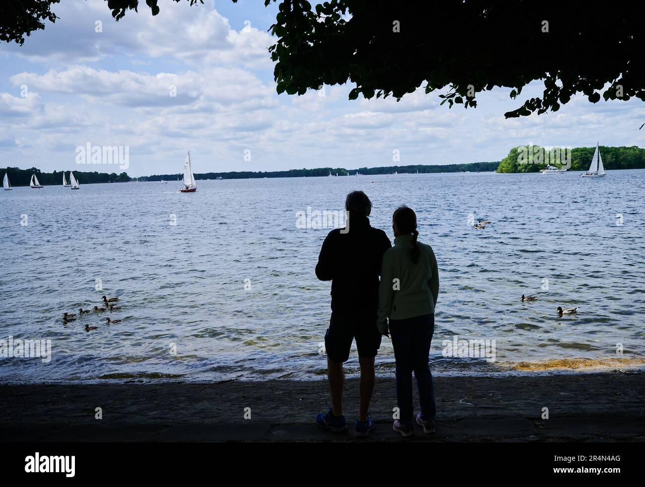 Berlino, Germania. 29th maggio, 2023. Una coppia si trova sulla riva del lago Tegel, sul quale una famiglia di anatre e barche a vela nuotano. Il bel tempo del lunedì di Pentecoste attrae molte persone al lago. Credit: Annette Riedl/dpa/Alamy Live News Foto Stock