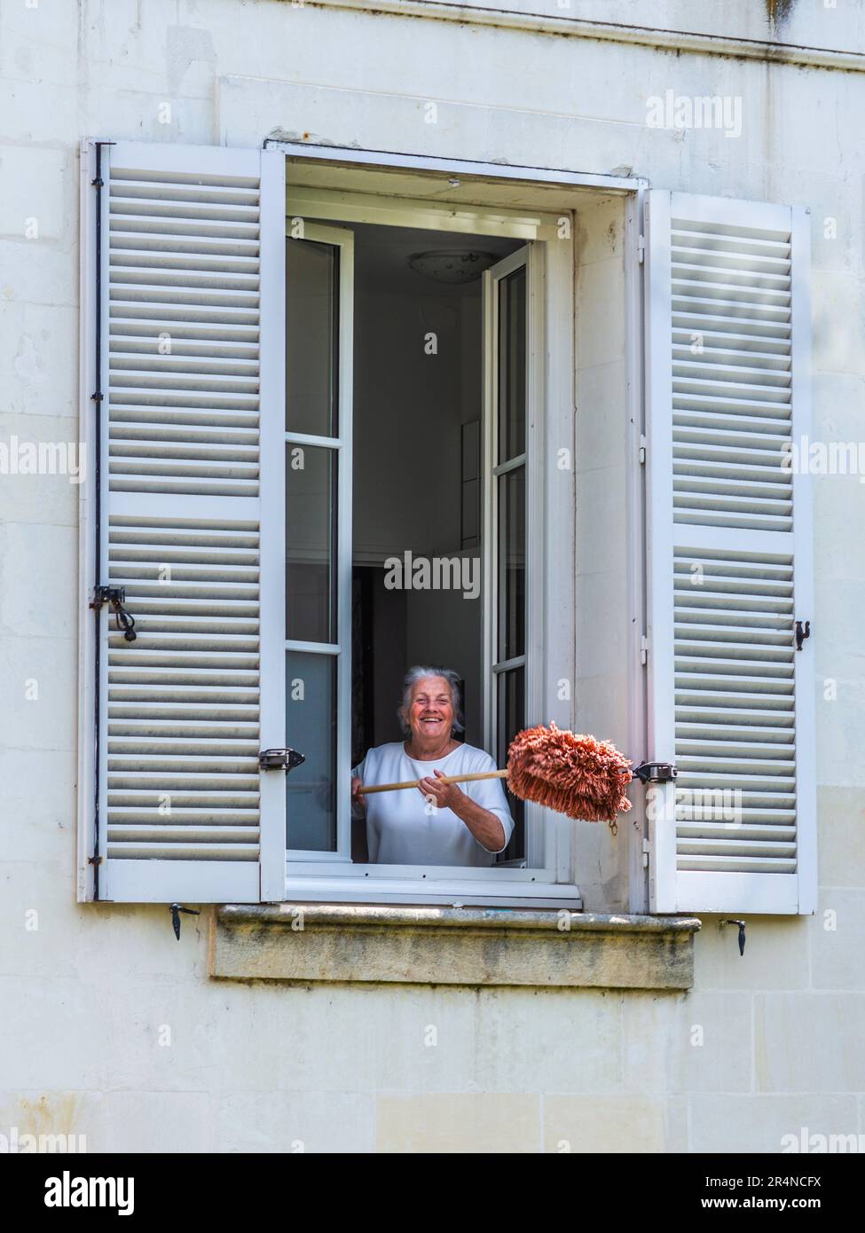 Donna matura che scuote spazzolone polveroso fuori dalla finestra aperta - Loches, Indre-et-Loire (37), Francia. Foto Stock