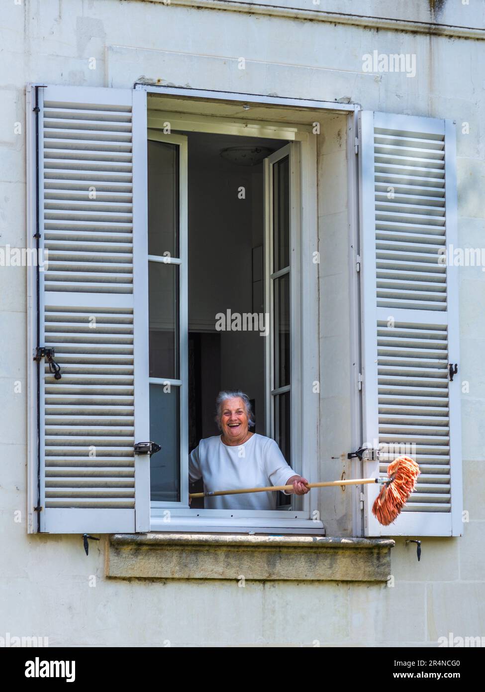 Donna matura che scuote spazzolone polveroso fuori dalla finestra aperta - Loches, Indre-et-Loire (37), Francia. Foto Stock