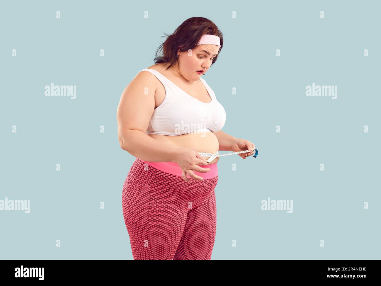 Donna in sovrappeso con pancia grassa guarda a misurare il nastro con l'espressione del viso sorpreso Foto Stock