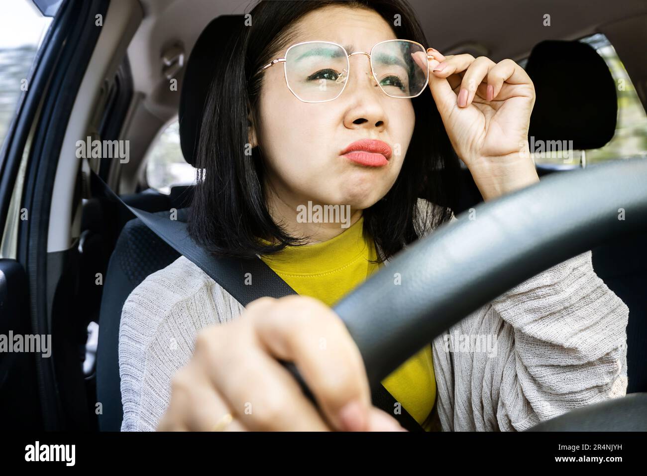 Concetto proibito e pericoloso con la donna asiatica lotta per guidare a causa di visione sfocata, mani che si aggrappano occhiali, e vietato la guida Foto Stock