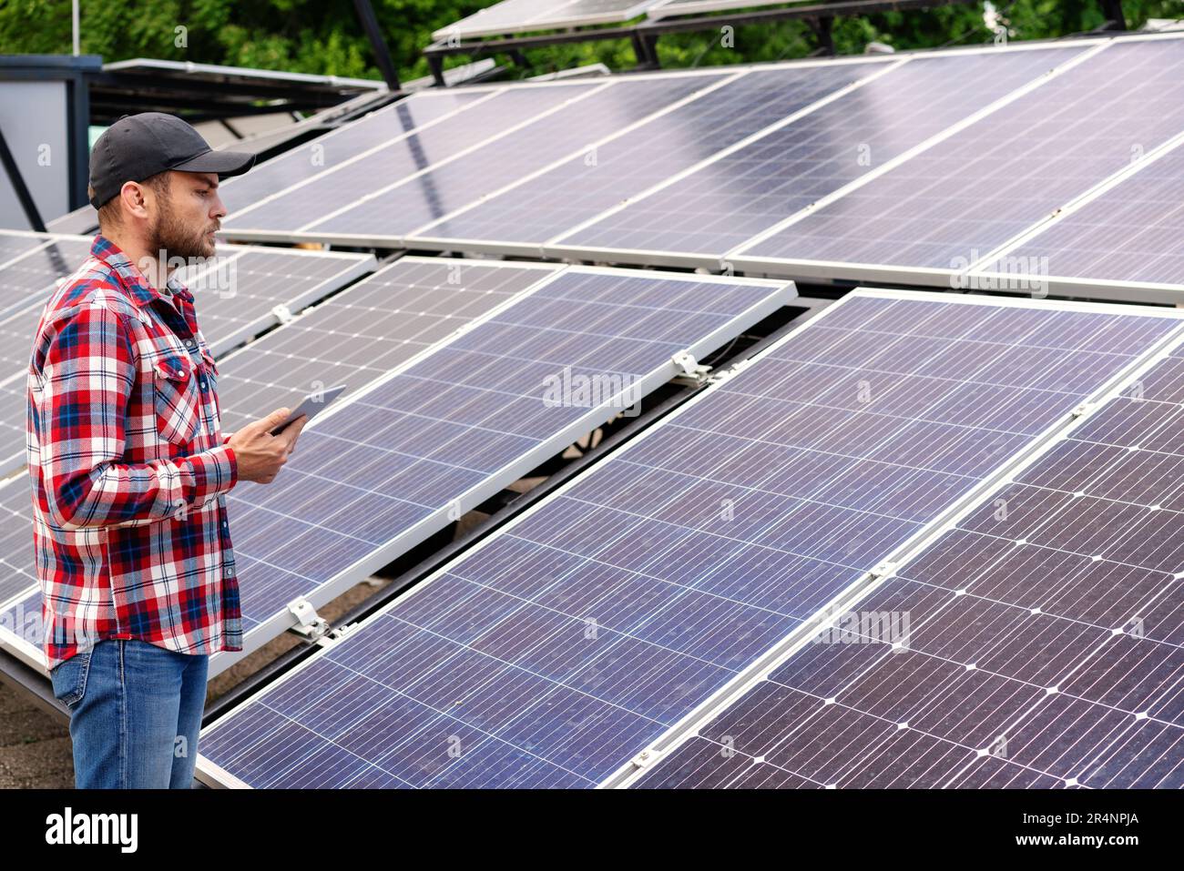 Lavoratore di una stazione di energia solare che tiene un tablet digitale e guarda i pannelli solari. Foto Stock