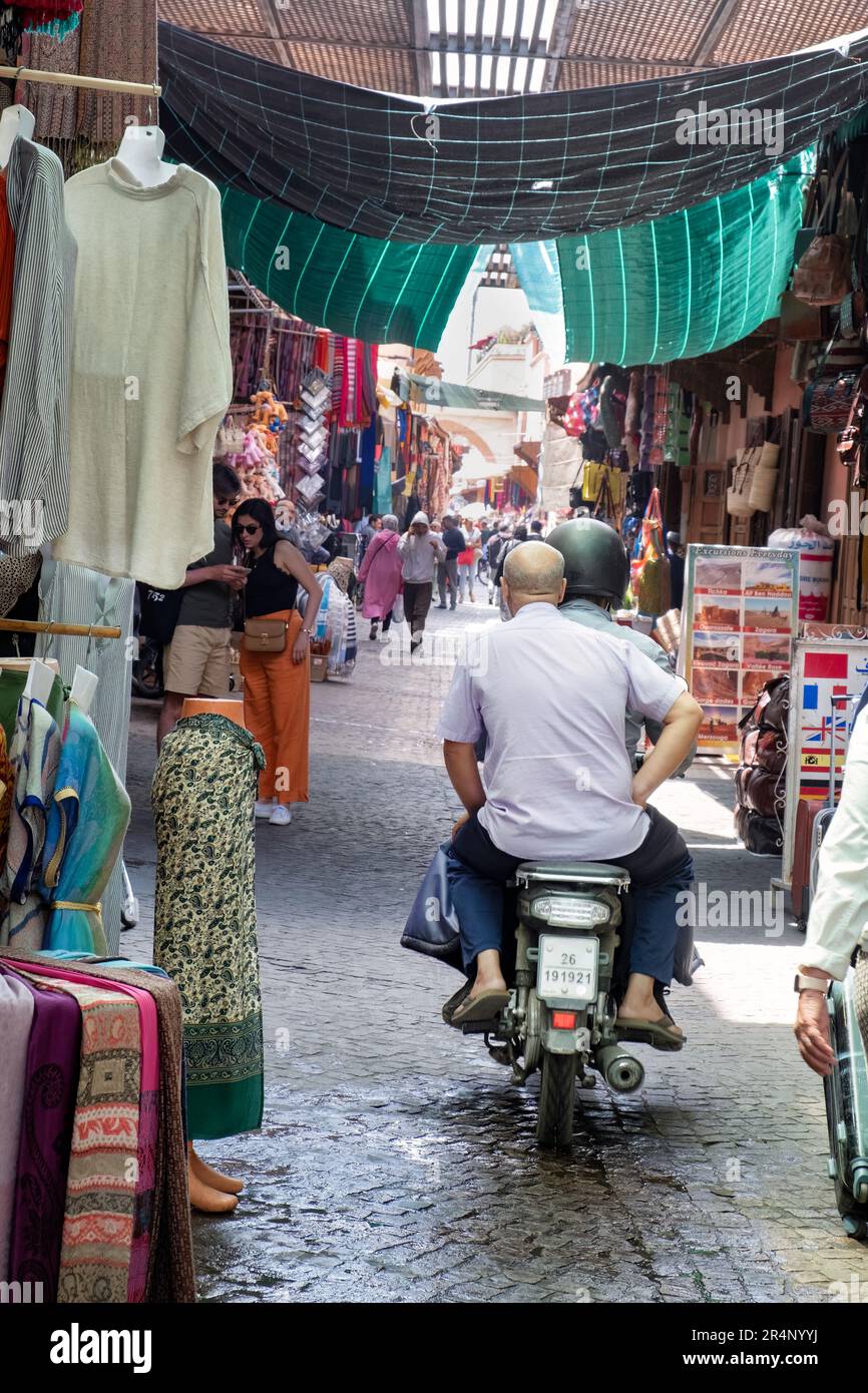 Una moto che viene guidata lungo uno stretto vicolo tra souk, occupato da acquirenti e pedoni nella zona centrale Souk di Marrakech marocco. Foto Stock