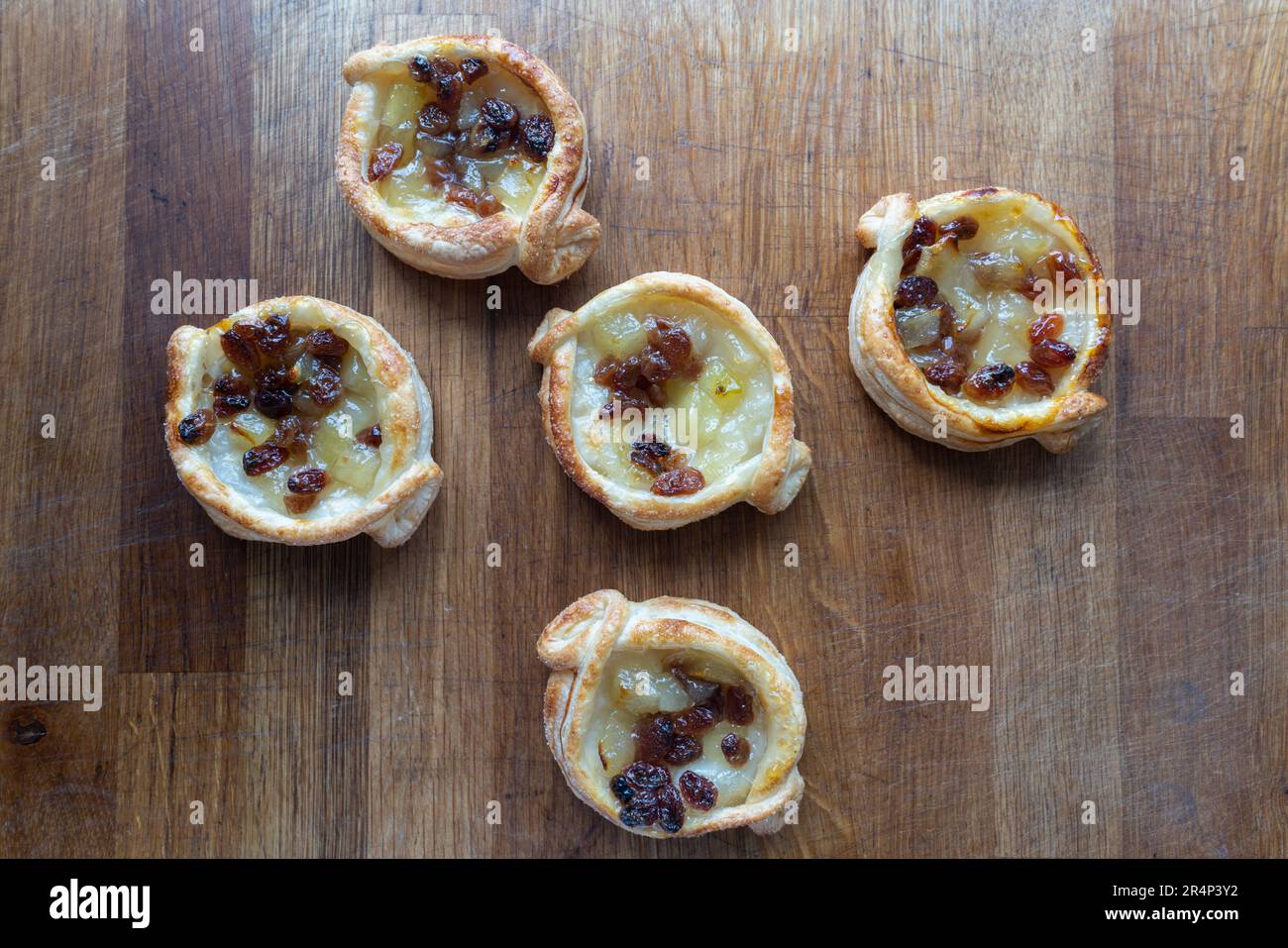 Un delizioso assortimento di dolci danesi al puff con una deliziosa combinazione di mela e uva sultanina, splendidamente sistemati su un rustico choppi di legno Foto Stock