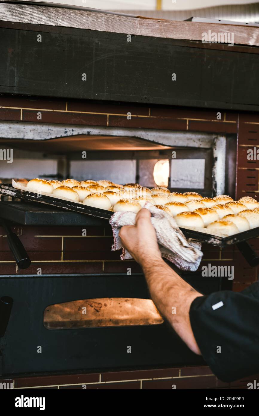 Panettiere irriconoscibile che togli dal forno il vassoio con pani gustosi. Foto Stock