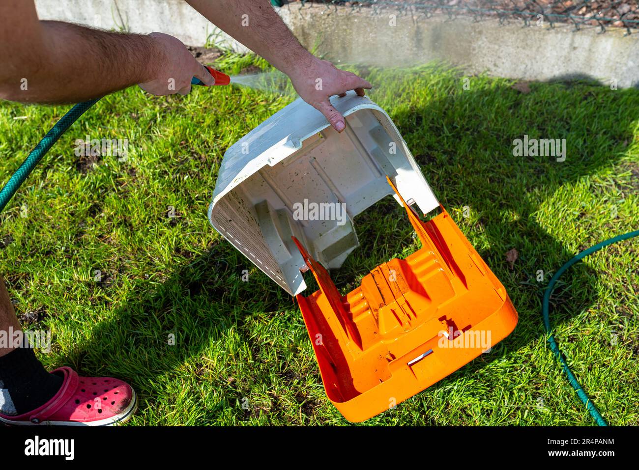 Un uomo lava con acqua un cestello del rasaerba sporco. Foto Stock