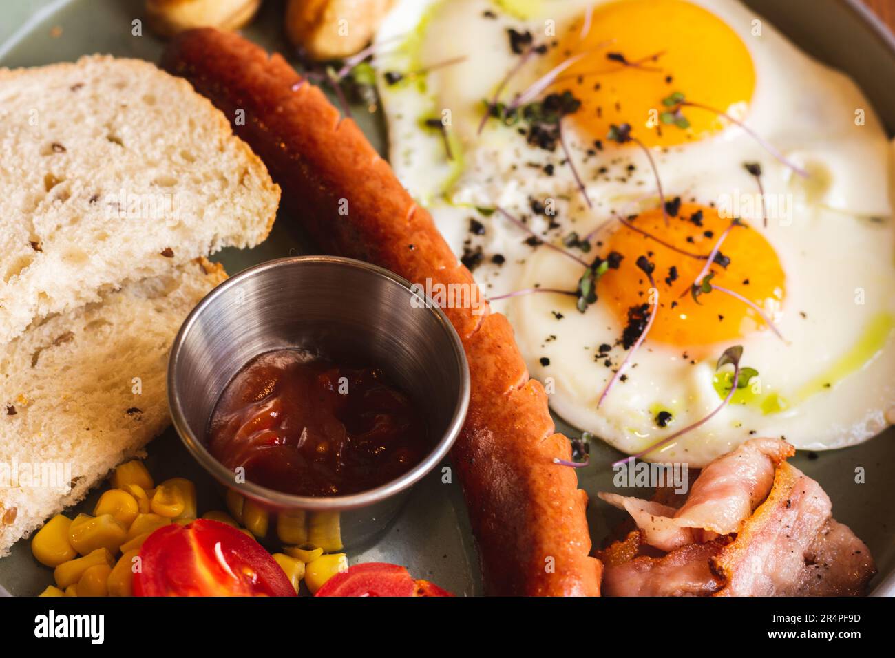 Uova fritte con salsicce, pomodoro e pane sul piatto. Colazione inglese nel caffè. Tavolo europeo per la colazione. Uova con carne e verdure. Foto Stock