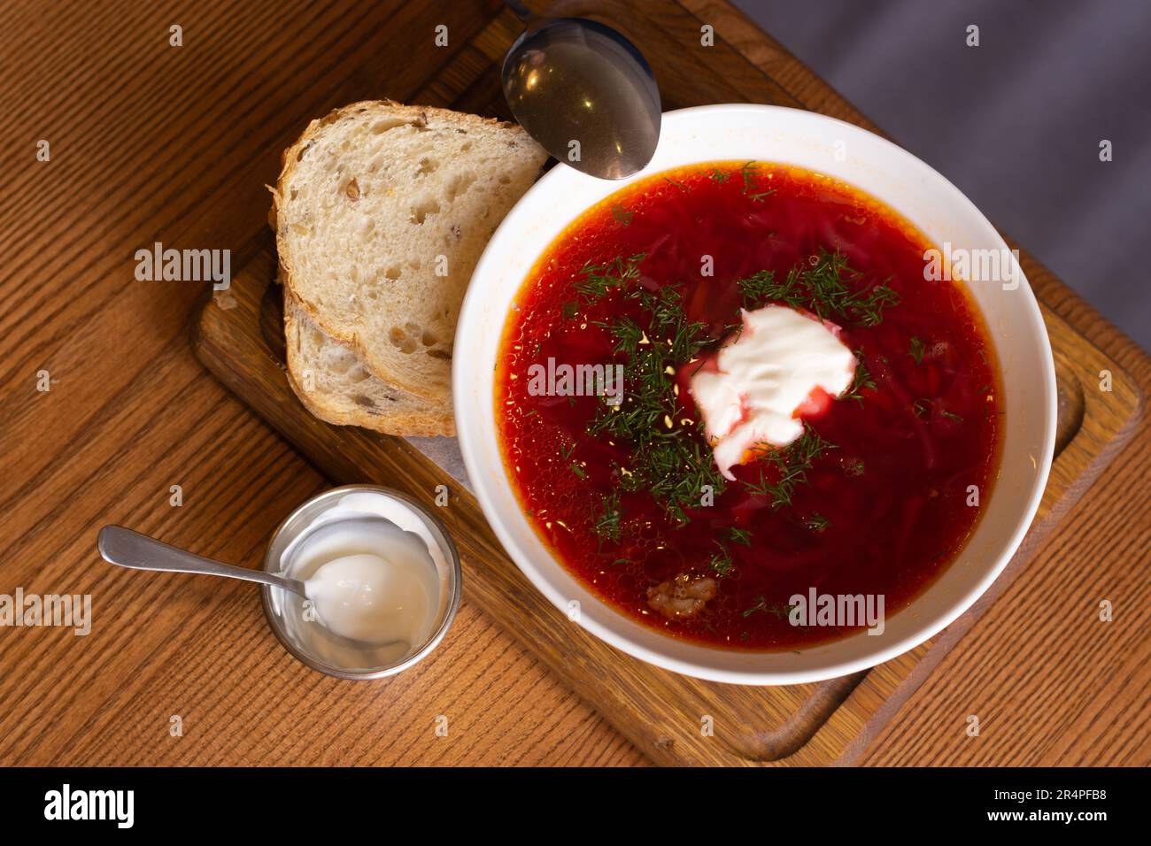 Borsone ucraino con pane su tavola di legno. Zuppa rossa con panna e pane. Ucraino cibo tradizionale. Borscht fatto in casa. Zuppa di pomodoro per cena. Foto Stock