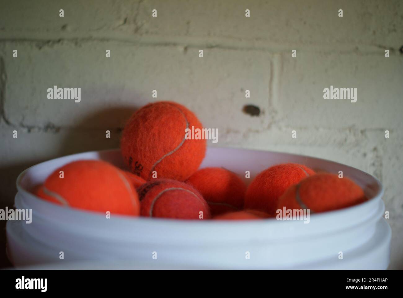 Palle da tennis arancioni traboccanti su una vasca bianca nel mobile costruito in mattoni per attrezzature sportive club. Tennis arancione florescente immagazzinato in un secchio bianco. Foto Stock