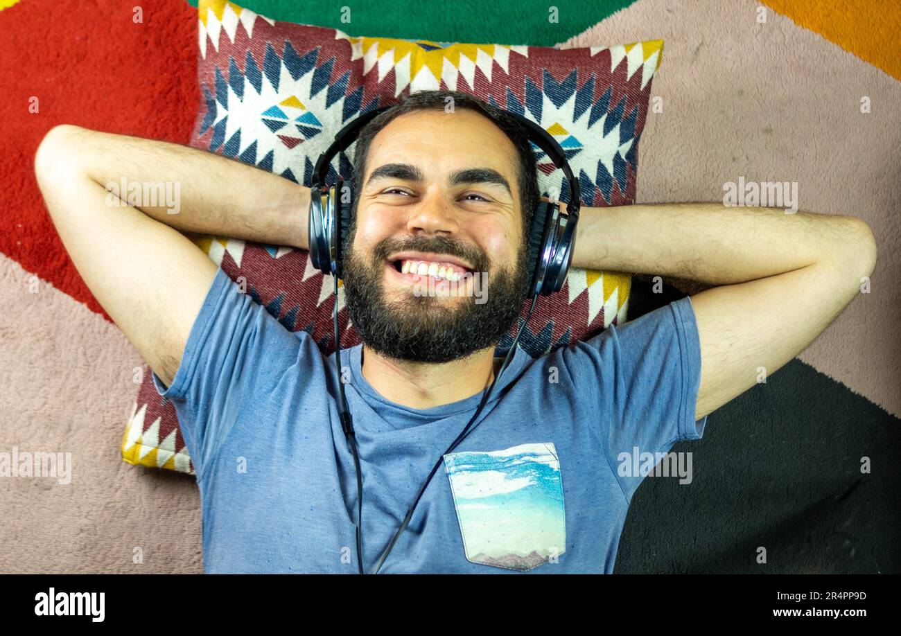 giovane uomo bearded usando le cuffie mentre sdraiato su un tappeto colorato Foto Stock