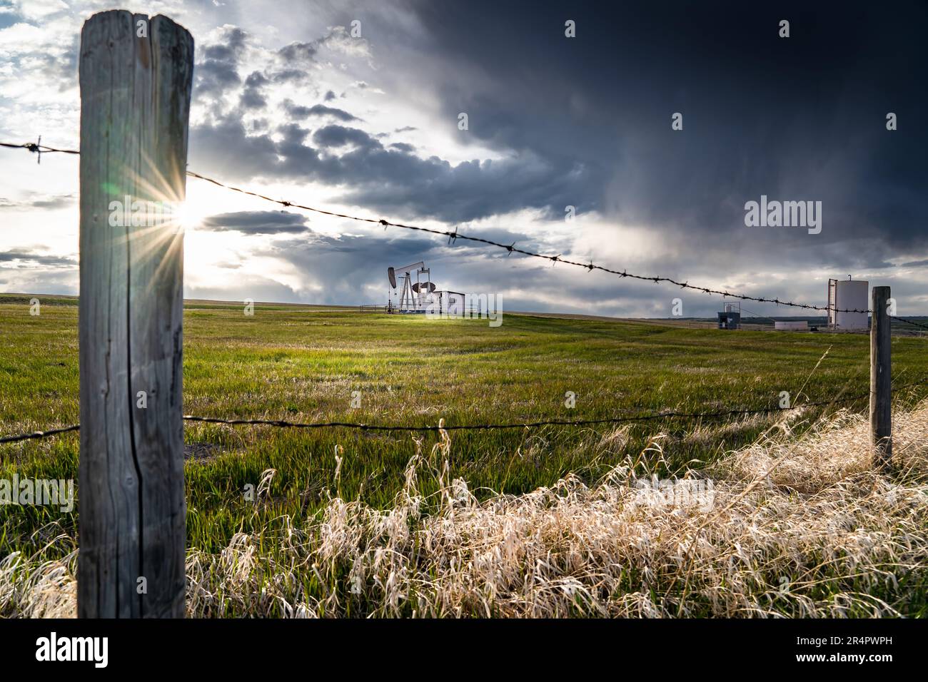 Scenario paesaggistico Prairie con recinzione in filo spinato che si affaccia su una presa distante pompa di olio sotto un cielo tempestoso in Rocky View County Alberta Canada. Foto Stock Scenario paesaggistico Prairie con recinzione in filo spinato che si affaccia su una presa distante pompa di olio sotto un cielo tempestoso in Rocky View County Alberta Canada. Foto Stock