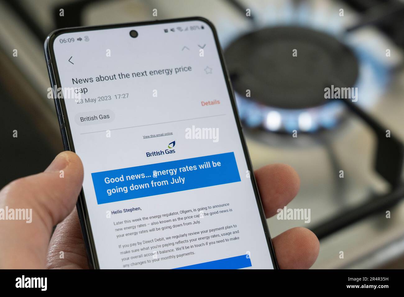 Mano di un uomo che tiene uno smartphone con un'e-mail di British gas sul nuovo limite del prezzo dell'energia nel luglio 2023. Un piano cottura a gas sta bruciando in background. REGNO UNITO Foto Stock