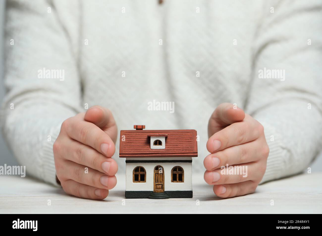 Concetto di sicurezza domestica. Uomo con modello di casa a tavolo di legno bianco, guardaroba Foto Stock