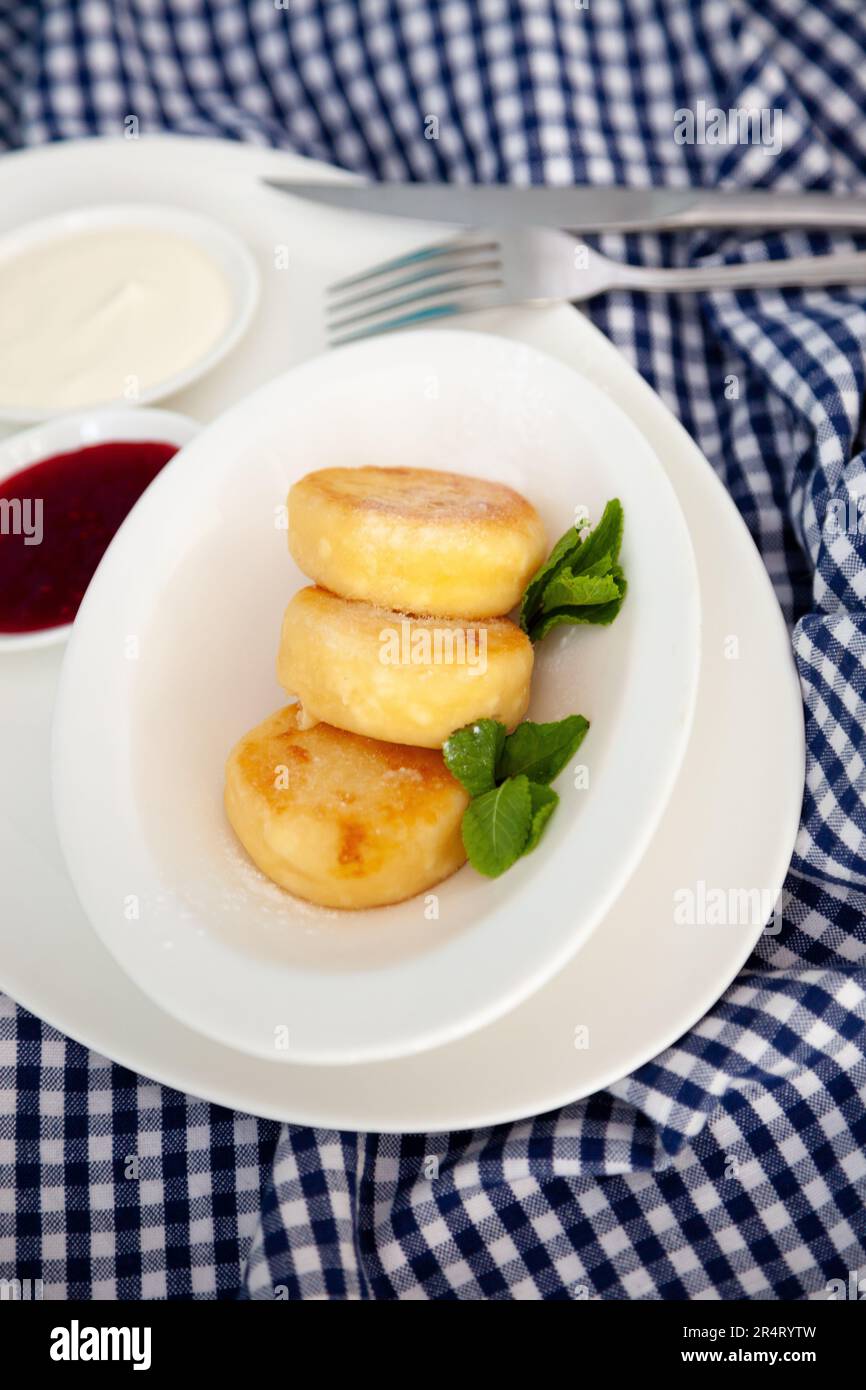 Frittelle di formaggio ricotta rotonda in un piatto bianco su sfondo blu. Cibo prima colazione. Cibo sano. Salsa di panna acida e menta. Primo piano vista dall'alto. Pasto dessert. Frittelle di ricotta al formaggio ricotta. Foto Stock