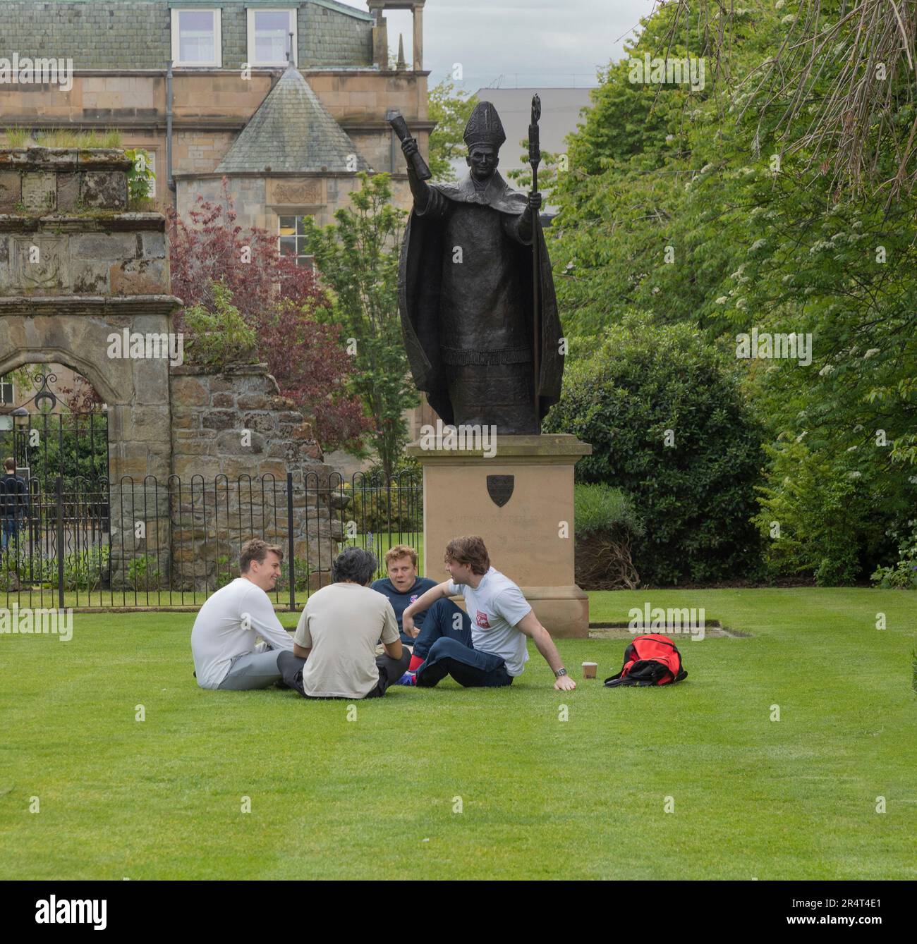 Quattro studenti maschi che si rilassano sotto la statua del vescovo Henry Wardlaw (2013, David Annand), nel quadrilatero del St Mary's College nel centro di St Andrews Foto Stock