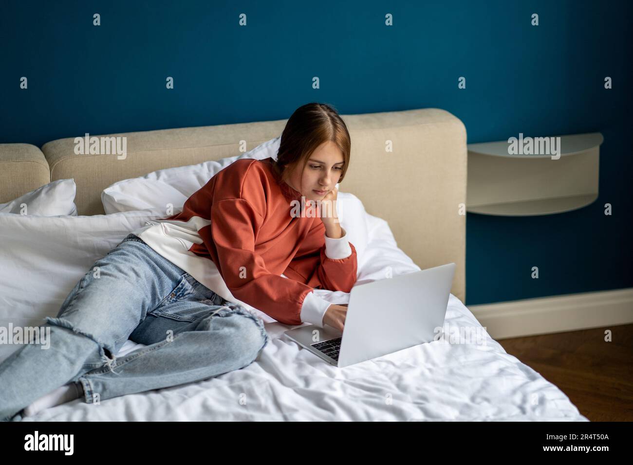 Pensieroso studente ragazza teen interessata sdraiato sul letto uso laptop studio online webinar a casa Foto Stock