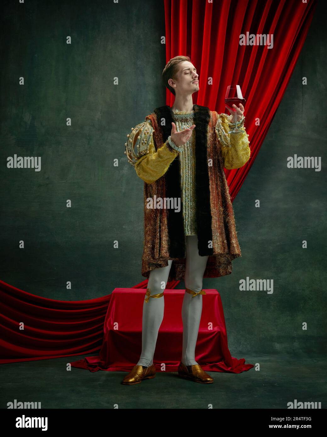 Ritratto di giovane duca, principe, reale in costume d'annata alzando il bicchiere di vino rosso su sfondo verde scuro, vintage Foto Stock