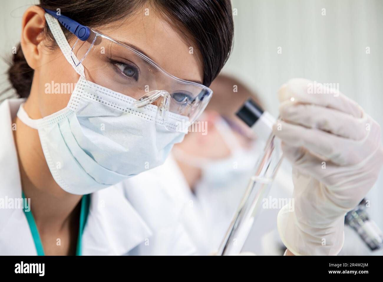Cinese donna asiatica femmina scienziato medico, ricercatore scientifico o medico guardando una provetta di liquido chiaro in una ricerca medica di laboratorio o di labo Foto Stock