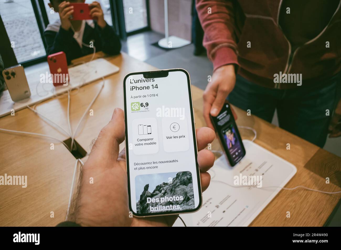 Parigi, Francia - 22 settembre 2022: Una persona tiene i nuovi computer Apple iPhone 14 in un negozio moderno, circondato dalla più recente tecnologia wireless - confrontare il dispositivo da 1019 euro - clienti in background Foto Stock