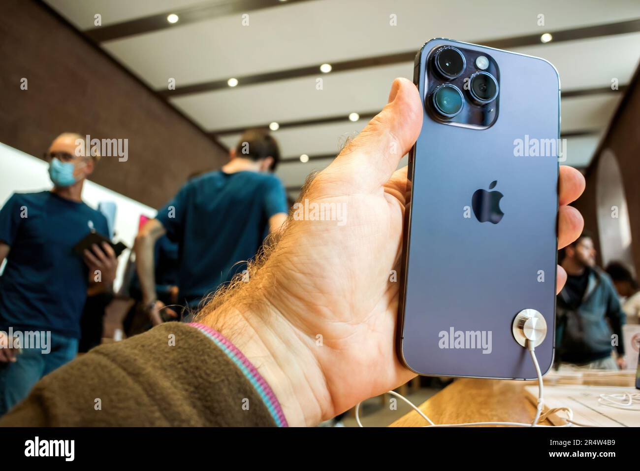 Parigi, Francia - 22 settembre 2022: Primo piano di una mano che tiene con fiducia il nuovo iPhone Pro 14 Max in un Apple Store, con i clienti in background. Foto Stock