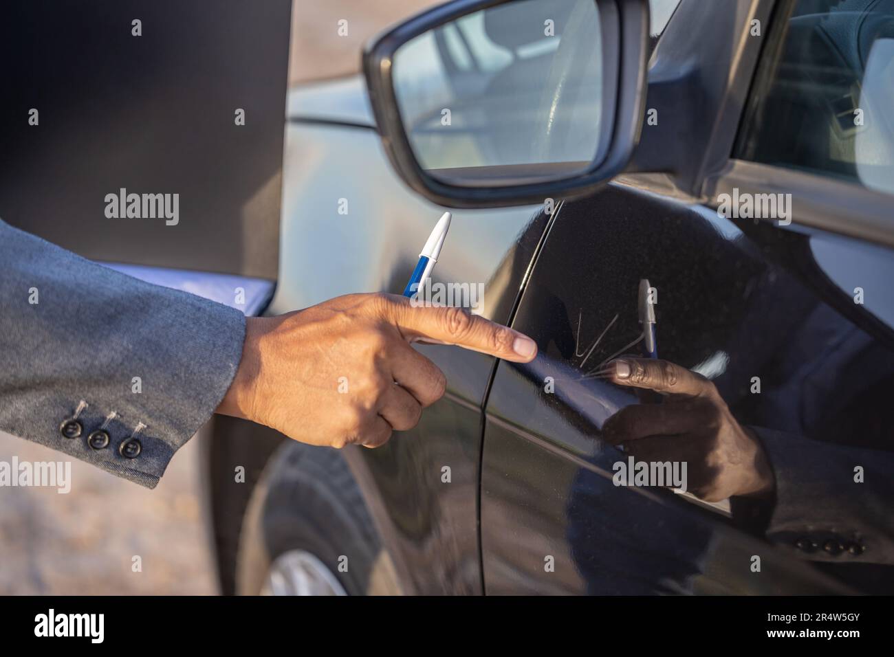 Dettaglio di una mano di un agente assicurativo che indica un graffio su un'auto. Foto Stock