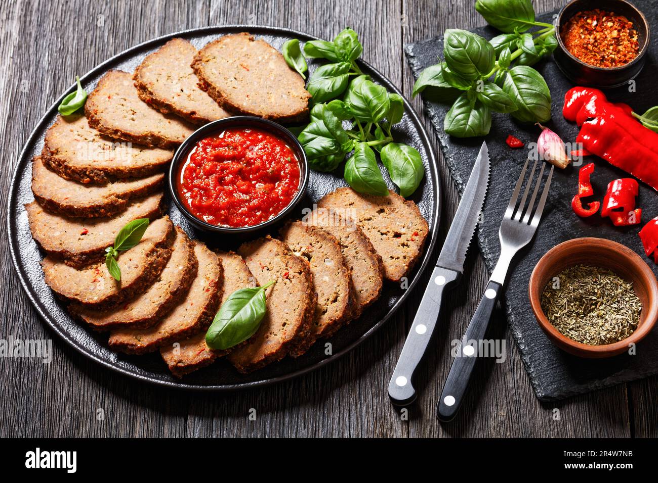polpettone italiano a fette con salsa di pomodoro e basilico fresco su piatto nero su tavolo di legno scuro Foto Stock