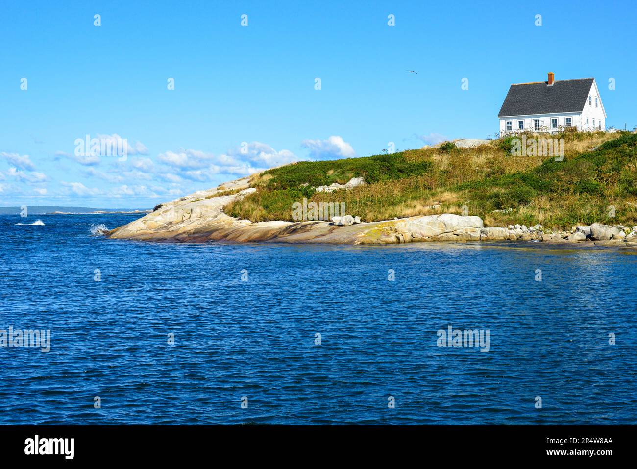 Una casa in legno bianca in stile rustico con numerose piccole finestre su una collina rocciosa. Le finiture dell'edificio sono di colore blu pallido con vista dell'oceano. Foto Stock