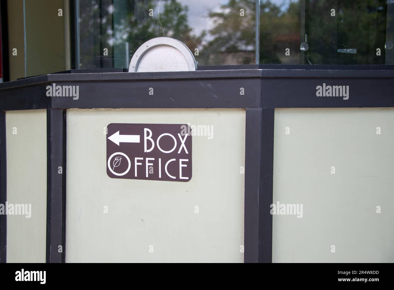 Una grande recinzione bianca con rifiniture nere e grandi alberi sullo sfondo. Il cartello ha uno sfondo marrone con lettere bianche. C'è una freccia. Foto Stock