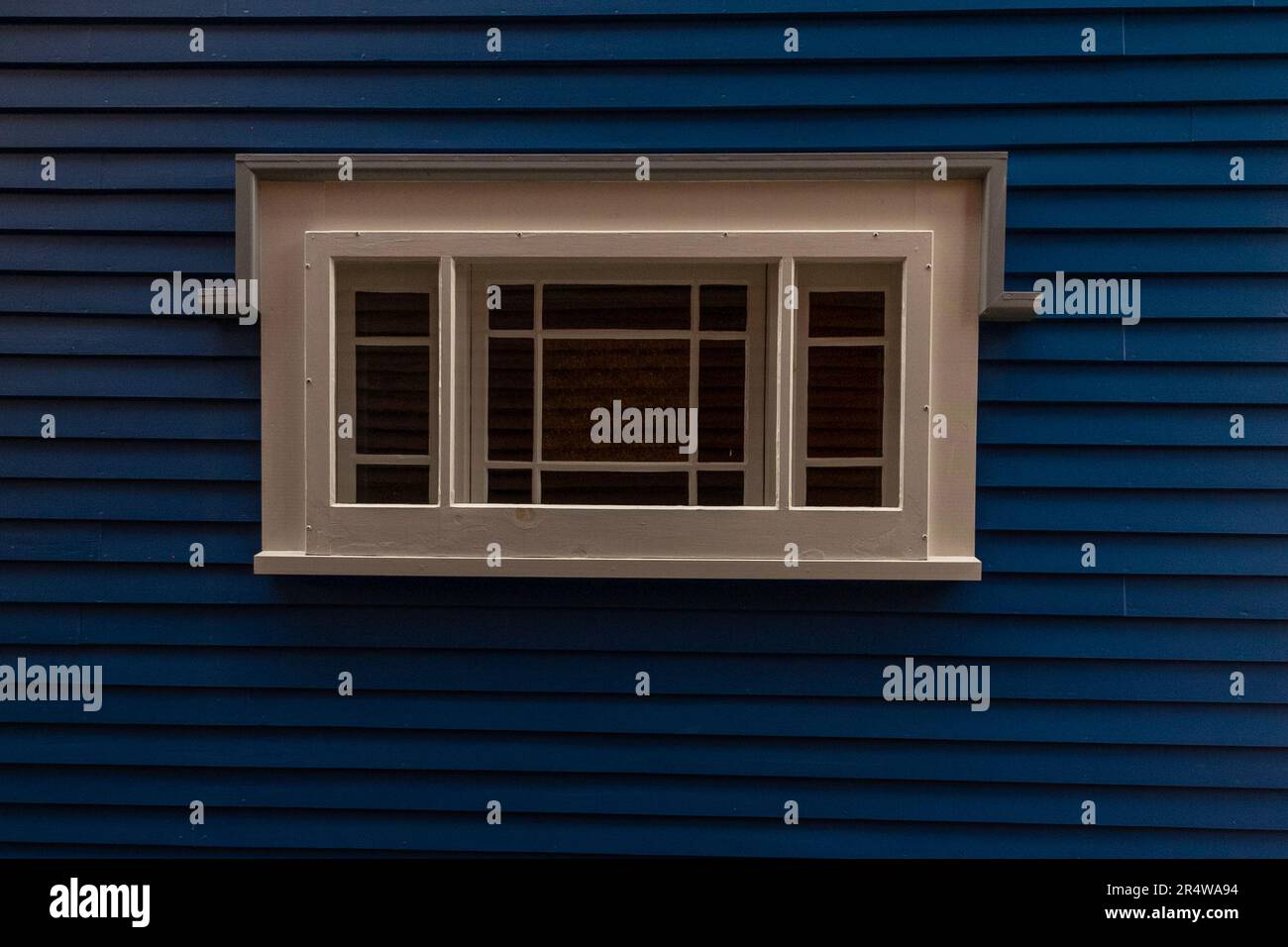 Una parete esterna dipinta di blu navy di una casa con uno stretto fianco in clapboard e una finestra in vetro trasparente d'epoca con mulloni tra i pannelli. Foto Stock