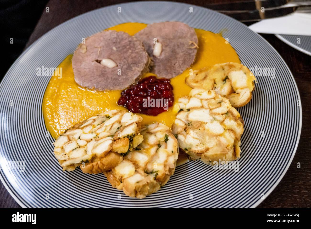 Bistecca di controfiletto, salsa di verdure e gnocchi carlsbad e marmellata di mirtilli rossi su piatto a strisce, primo piano. Specialità tradizionale della repubblica Ceca. Foto Stock