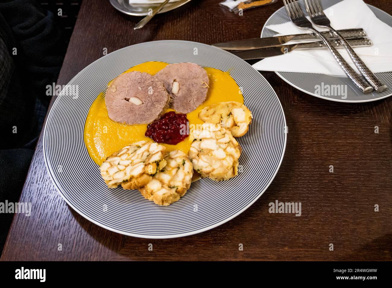 Bistecca di controfiletto, salsa di verdure e gnocchi carlsbad e marmellata di mirtilli rossi su piatto a strisce, cena al tavolo del ristorante. Specia tradizionale della repubblica Ceca Foto Stock