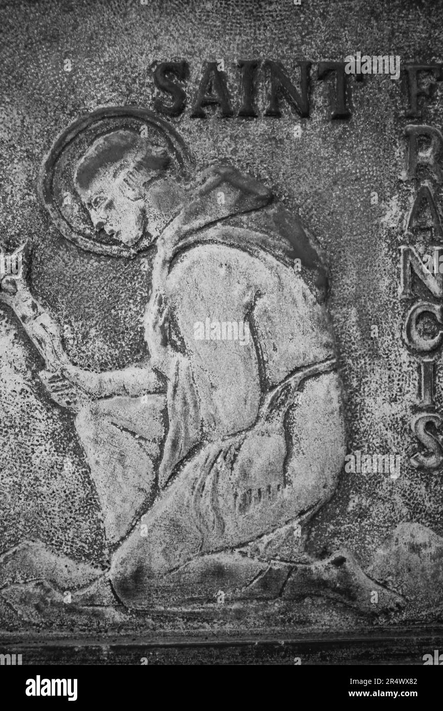 Un ritratto scolpito di San Francesco che si inchinava su un ginocchio in bianco e nero monocromatico. Foto Stock