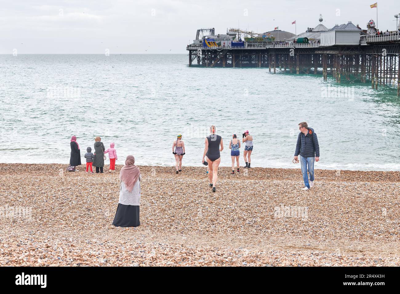 Un uomo guarda una donna in un costume da bagno in procinto di unirsi ad altre donne sulla riva presso il molo di Brighton, costa meridionale dell'Inghilterra, per una nuotata in una sorgente fredda Foto Stock