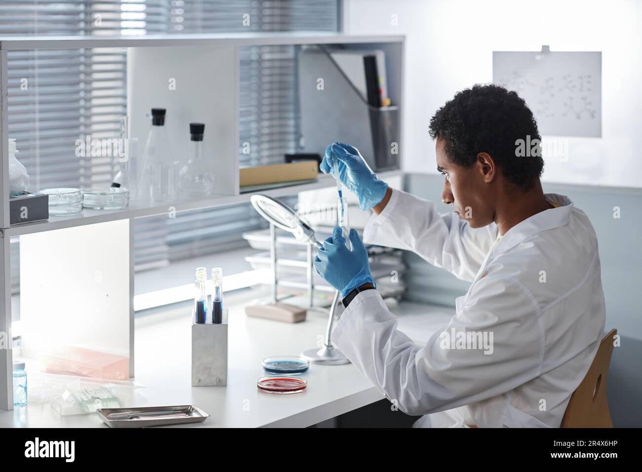 Vista laterale ritratto di giovane etnico che fa prove a workstation in moderno laboratorio, copia spazio Foto Stock