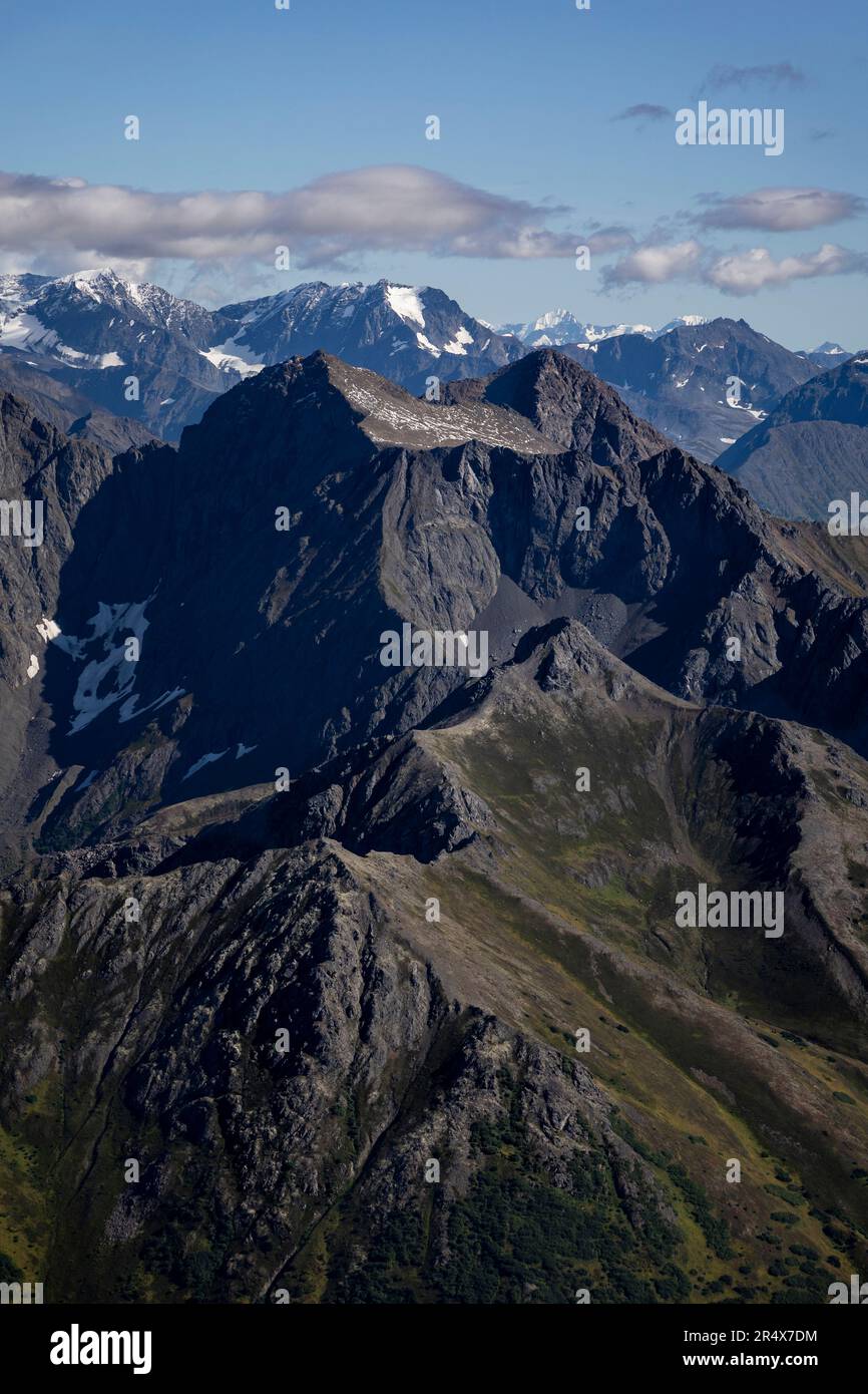 Vista aerea ravvicinata delle maestose vette della catena montuosa Chugach, con la dorsale innevata in lontananza contro un cielo blu nel ... Foto Stock