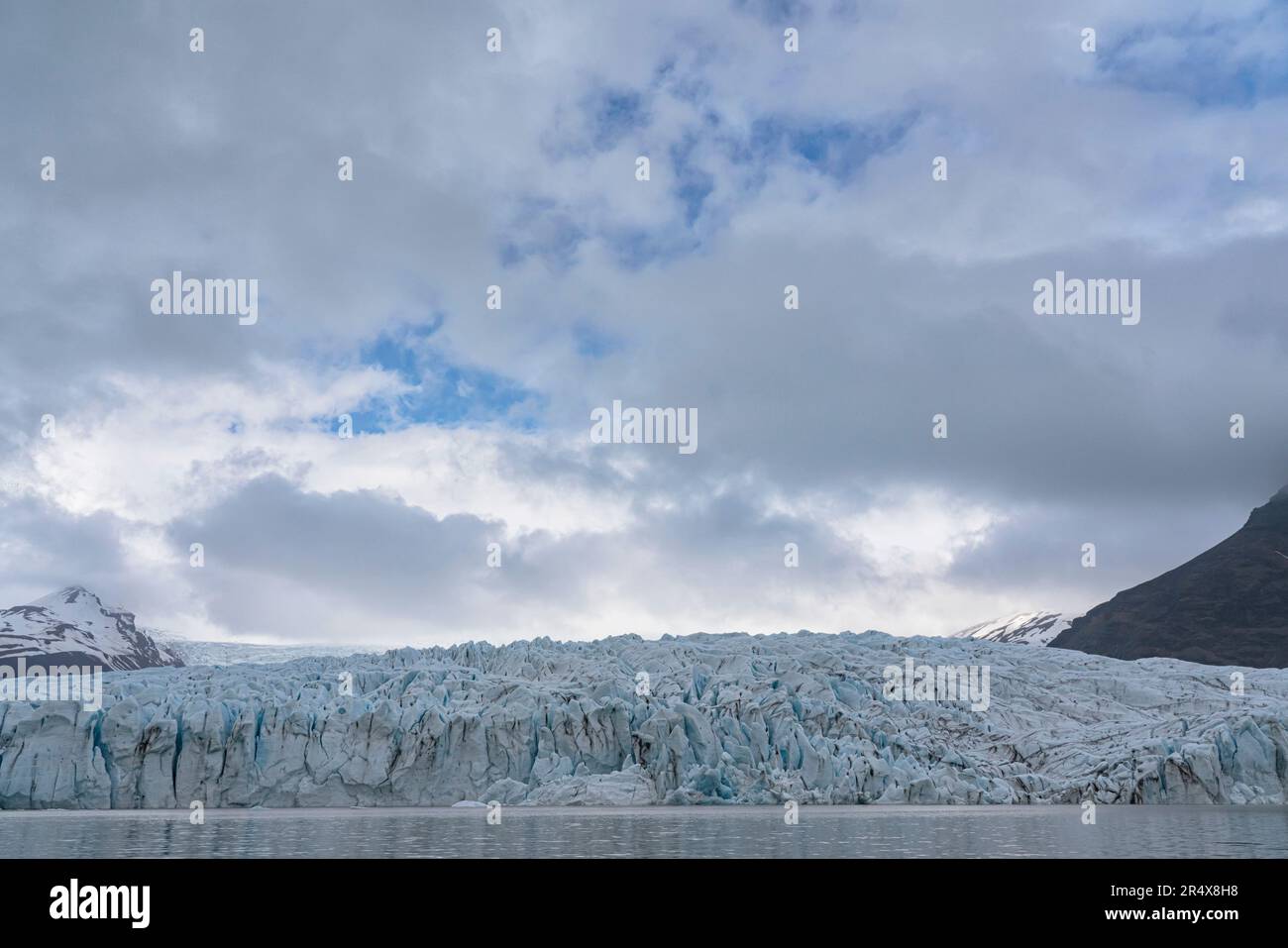 Vista dalla laguna del ghiacciaio Fjallsarlon del ghiaccio blu del capolinea del ghiacciaio Fjallsjokull che si erge contro le nuvole grigie che coprono... Foto Stock