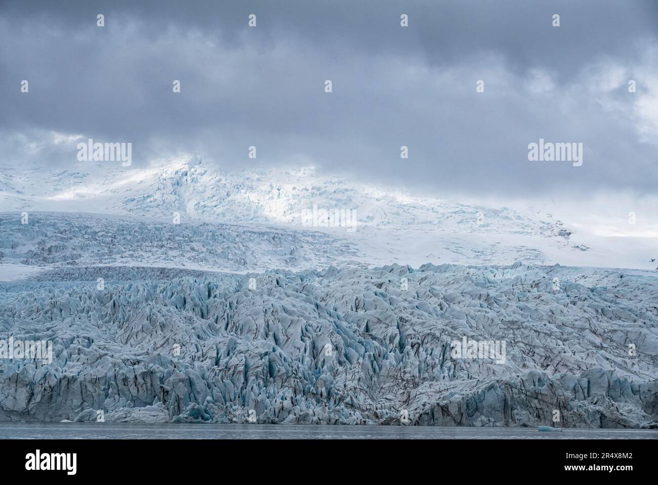 Le viste del ghiaccio blu del capolinea del ghiacciaio Fjallsjokull si stagliano contro le nuvole grigie e nebbiose, scattate dalla laguna del ghiacciaio Fjallsarlon al numero ... Foto Stock