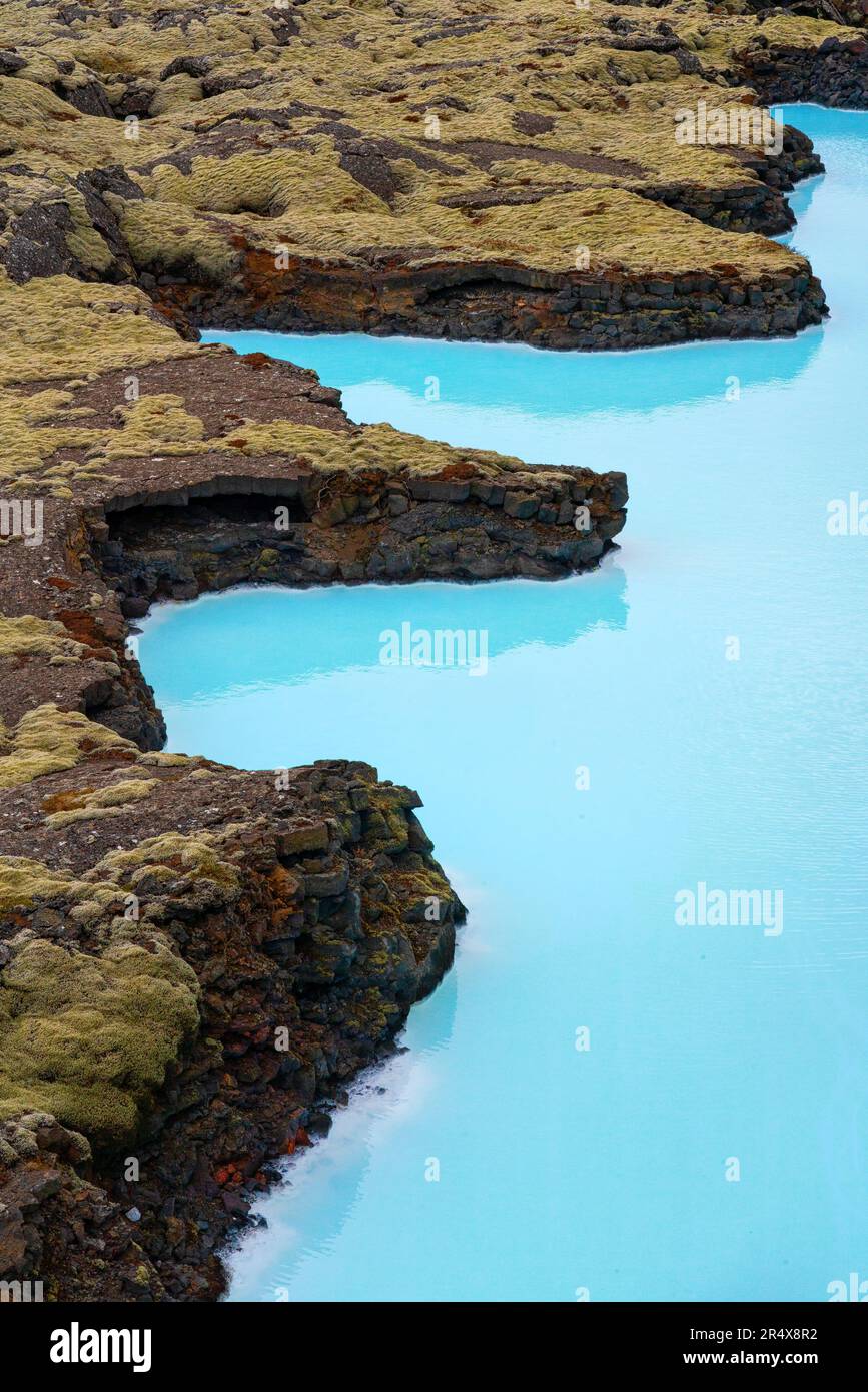 Splendida vista aerea dell'acqua blu turchese che crea un contrasto dinamico con i campi di lava coperti di muschio lungo la costa dell'Islanda meridionale Foto Stock