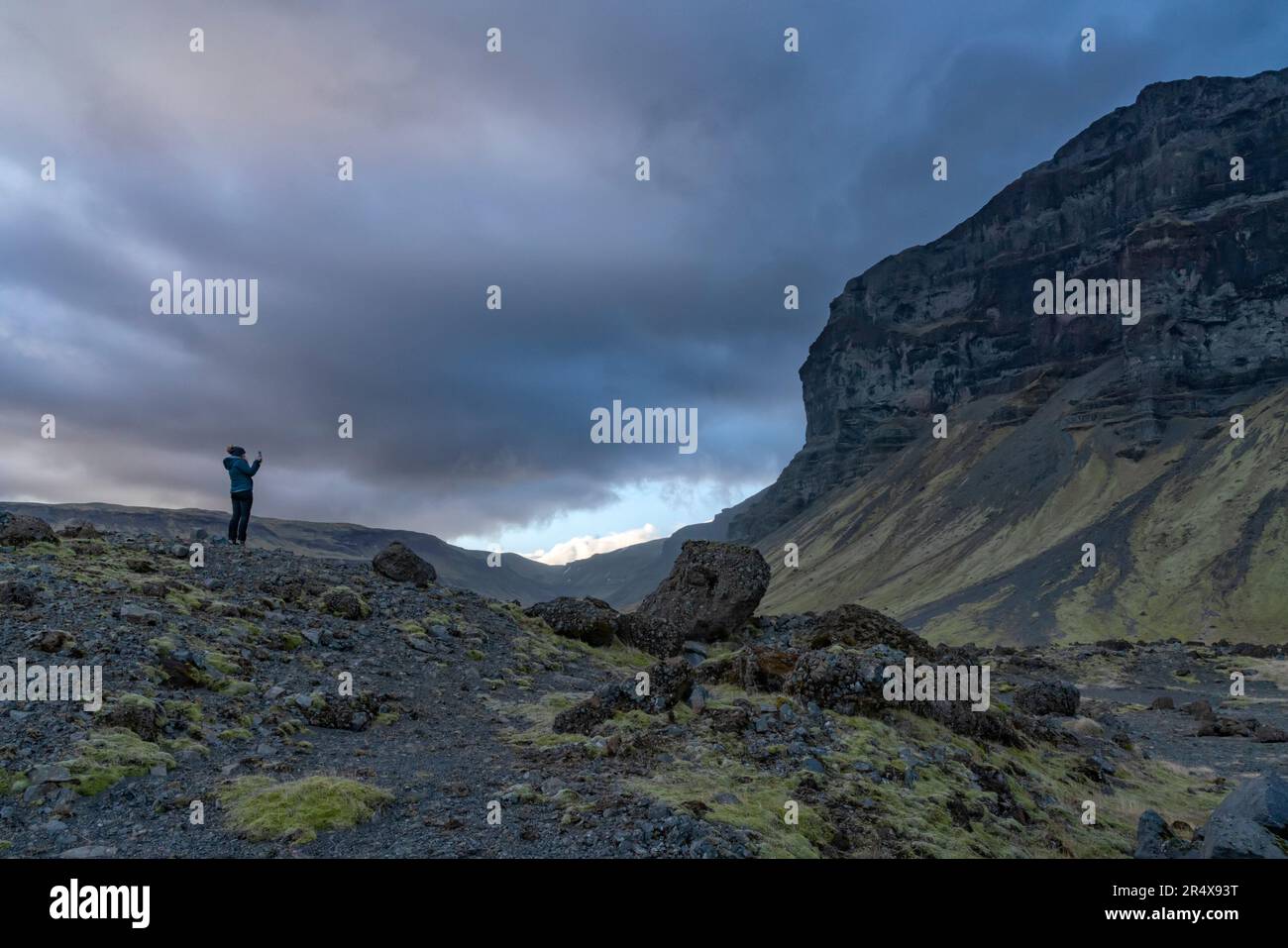 Donna in piedi sul paesaggio vulcanico e roccioso ammirando la bellezza naturale e scattando una foto delle montagne e delle spettacolari nuvole di tempesta per... Foto Stock