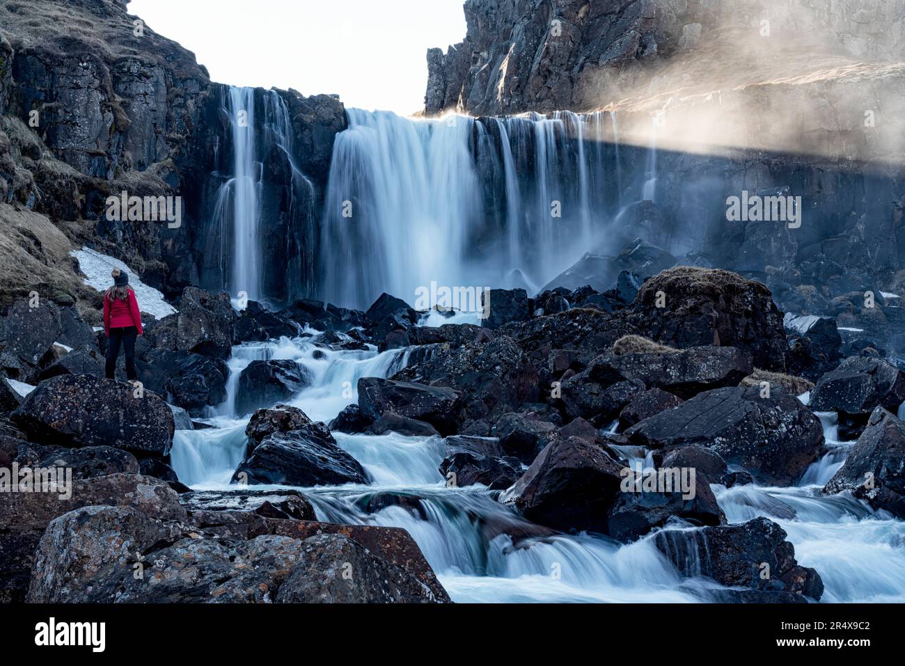 Donna in piedi vicino a una cascata appena fuori Seyðisfjörður nei fiordi orientali dell'Islanda; Islanda orientale, Islanda Foto Stock