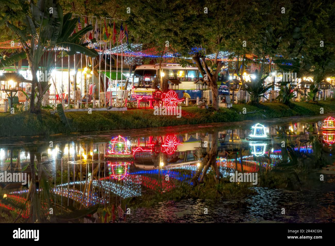 Le luci decorative della strada gettano i loro riflessi sulla superficie delle acque fangose del fiume che fluiscono attraverso Siem Reap. Foto Stock