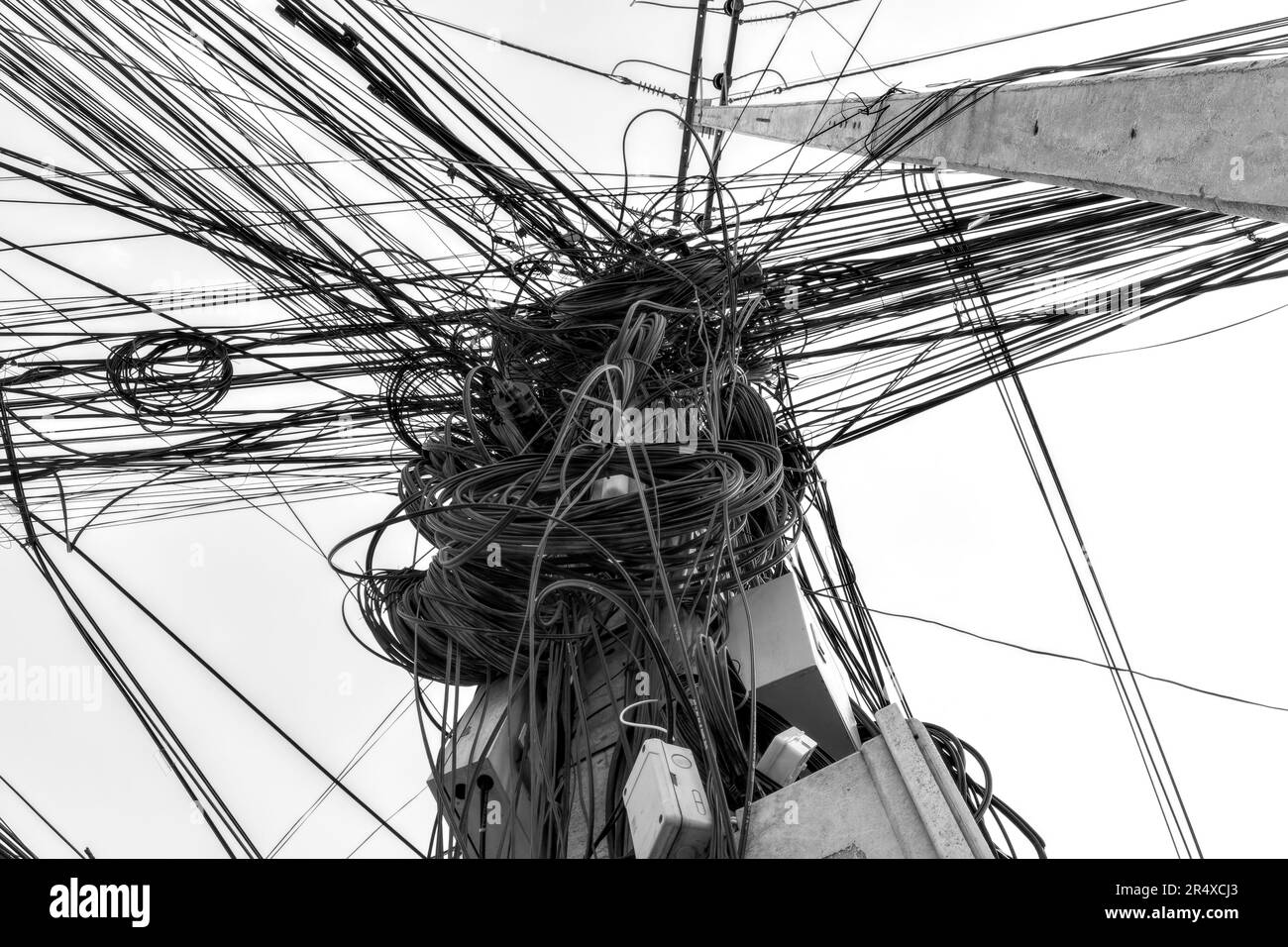 Un gruppo di fili e cavi impigliati su un palo, catturando l'intricata e caotica rete di linee elettriche asiatiche. Foto Stock