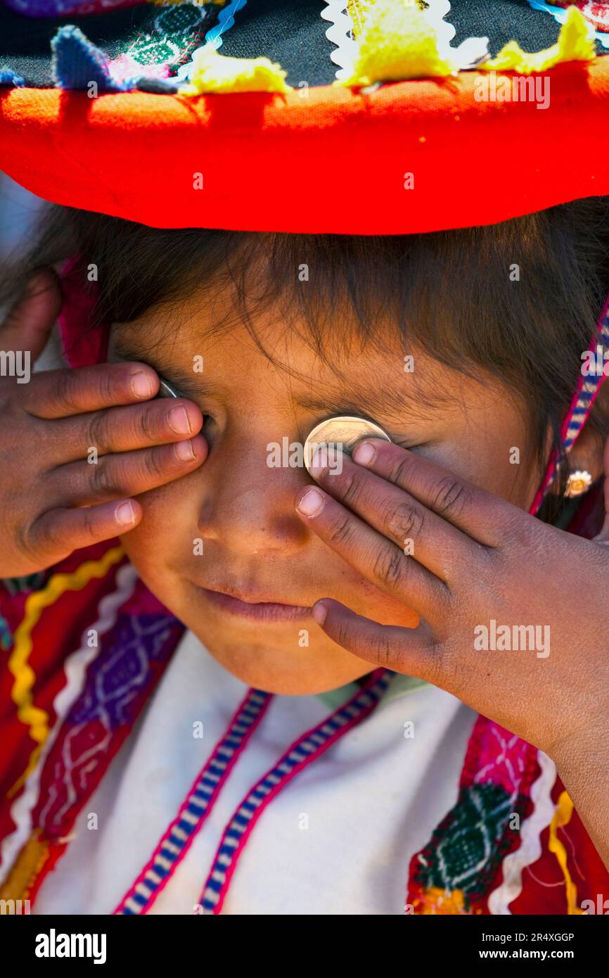 La giovane ragazza peruviana mette monete del valore di Dos Soles sugli occhi; Cuzco, Perù Foto Stock