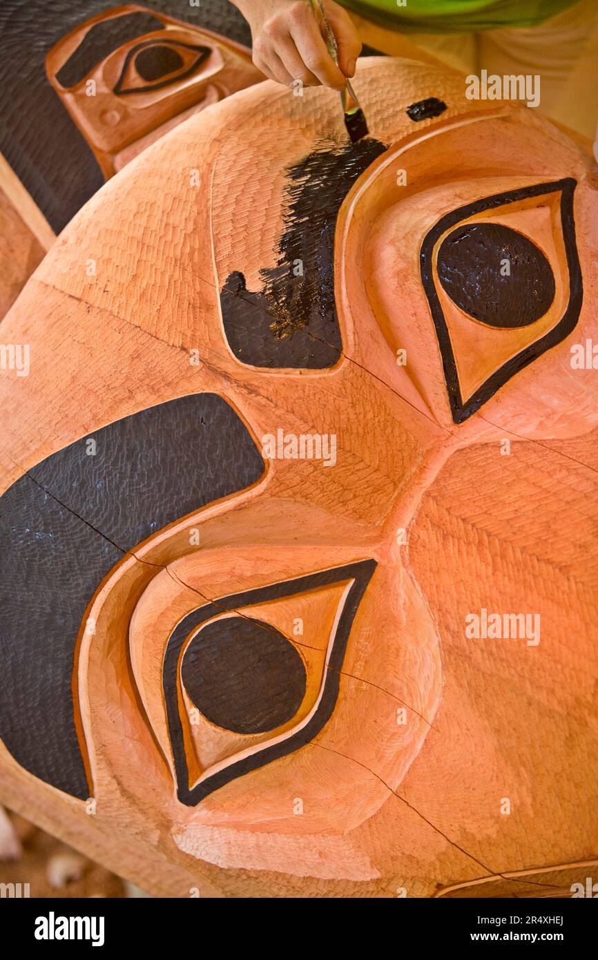 Tlingit Wood carver painting a totem in Saxman Totem Park, Ketchikan, Alaska, USA; Ketchikan, Alaska, Stati Uniti d'America Foto Stock