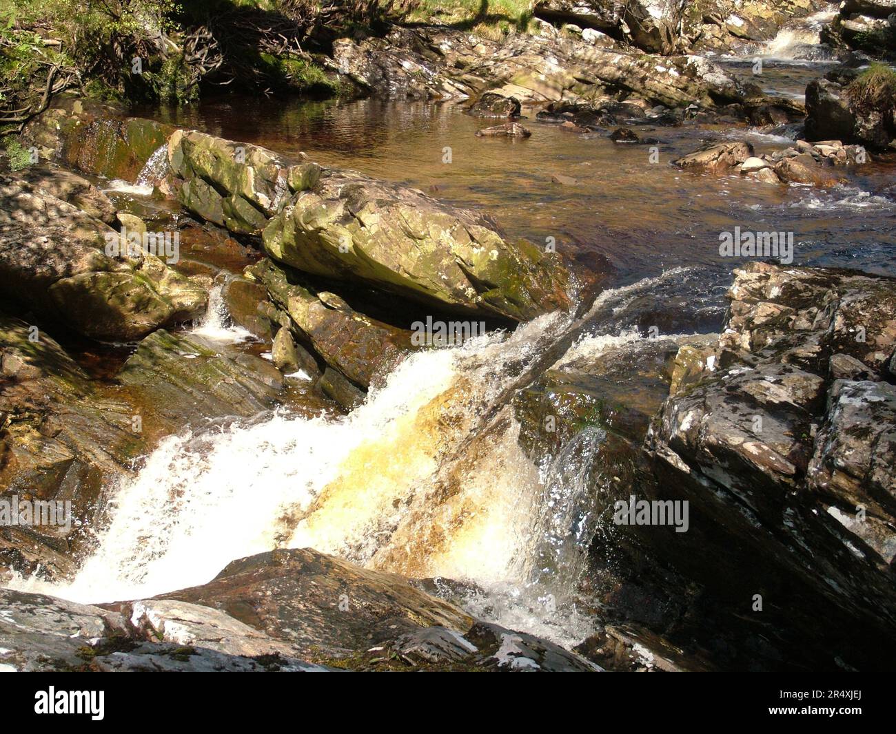 Acqua colorata di torba che scorre su una cascata formata dagli strati inclinati di antiche rocce di un torrente nelle Highlands della Scozia. Foto Stock